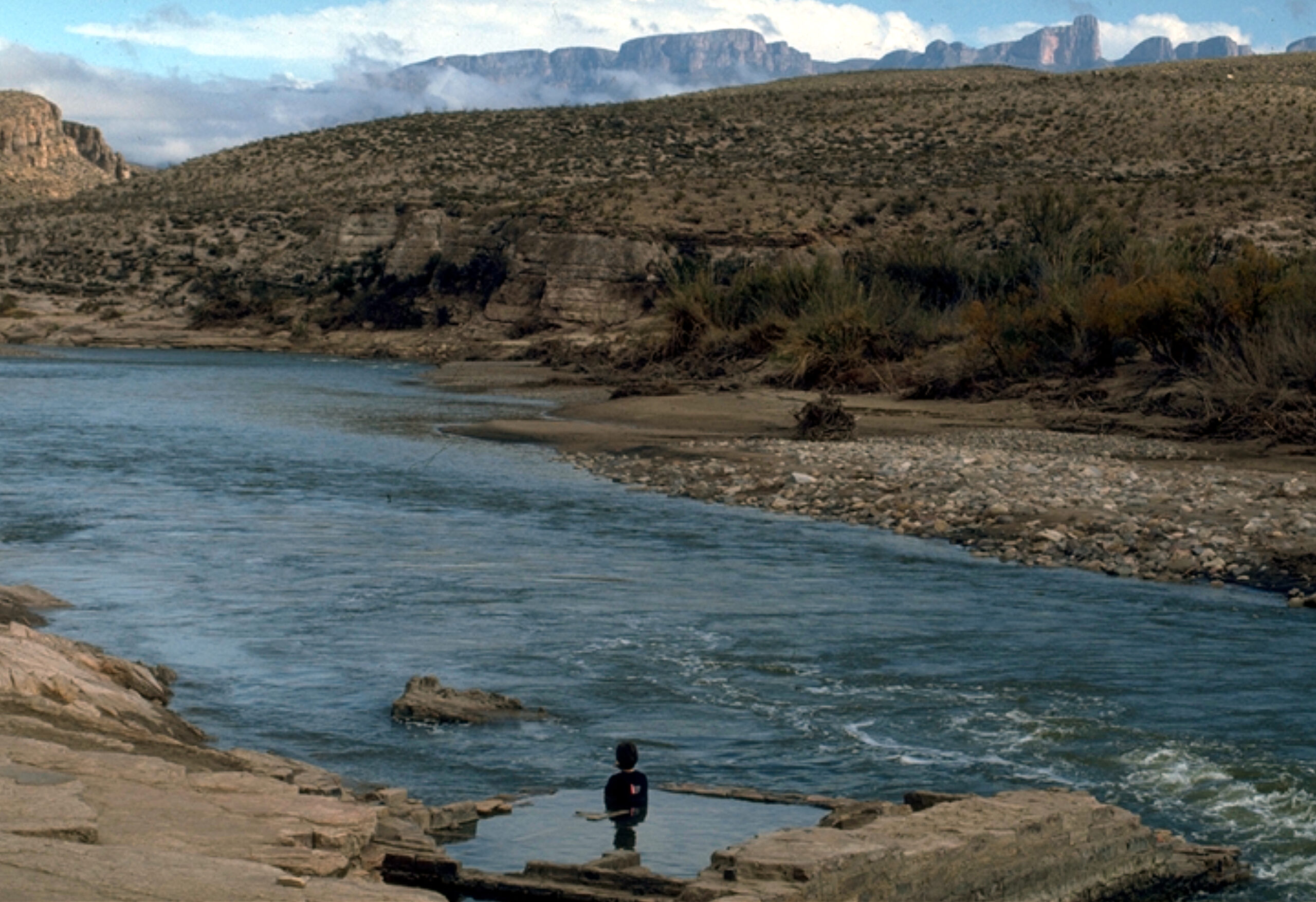 Guest sitting in the water in the ruins of the Hot Springs mineral baths on the Rio Grande river with the Sierra del Carmen mountains in the background